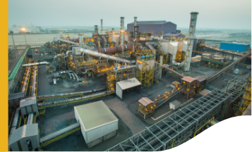 The image shows an industrial complex with various structures, including large buildings, chimneys, pipes, and machinery. The area appears to be a manufacturing or processing plant with multiple interconnected components and pathways.