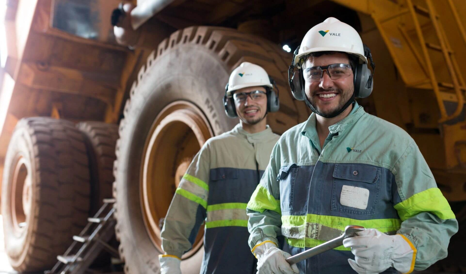 Two Vale employees with white helmets and ear protection smiling at the mining facility