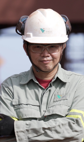 Image of a male employee smiling. He is wearing proctetion itens such as helmet and glasses.