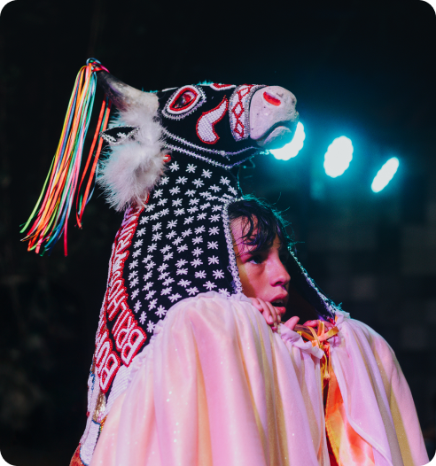 Person wearing traditional attire holding a bull mask during a nighttime cultural performance.