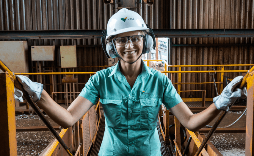 A Vale employee, in uniform and protective gear, smiles for a photograph. She is in an operational environment.