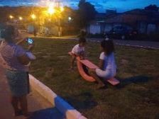 Nighttime image of two children playing on a seesaw while a woman photographs them.