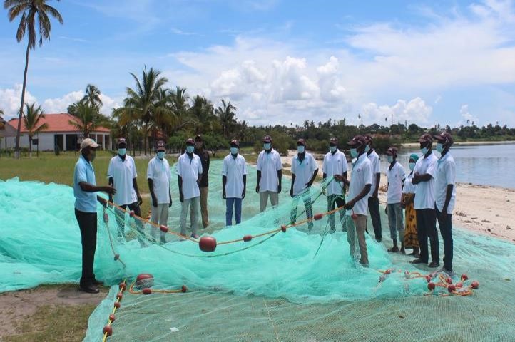 Several people, all in white, are around a large, pale green fishing net.