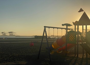 Image of the beach at sunset and some children's toys, such as swings.