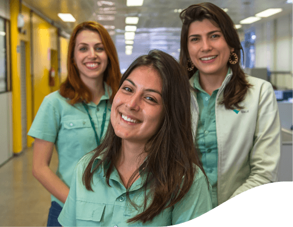Three women smiling in an office. The three with their hair down and wearing light green shirts.