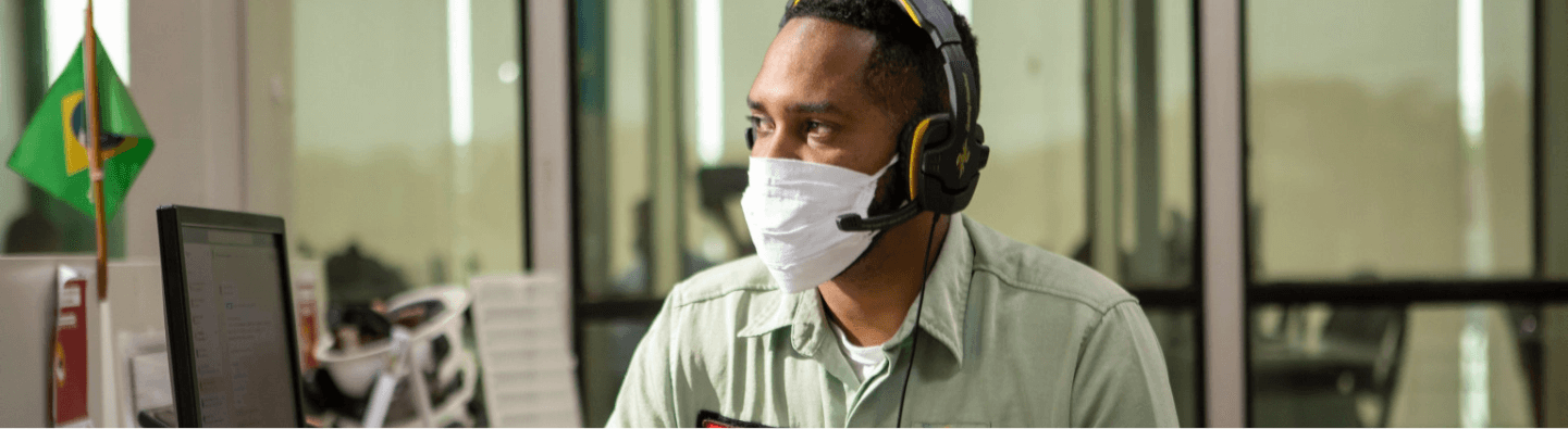 Man, wearing mask and headset with microphone, inside an office.