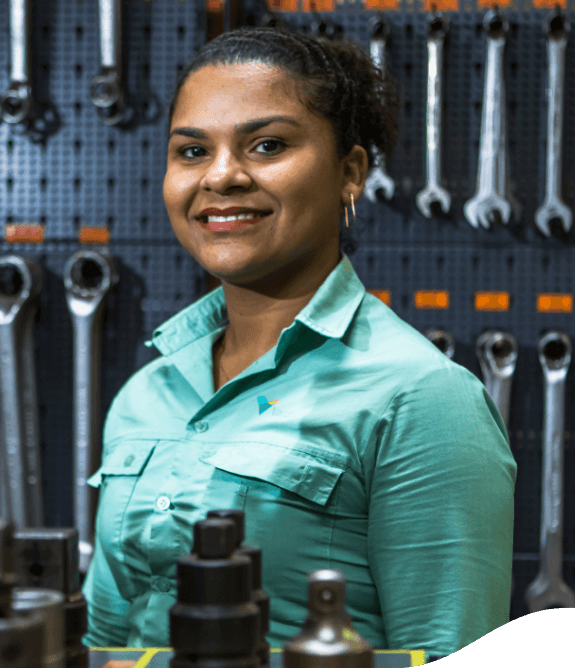 A black woman smiling in a space full of maintenance tools. She has her hair up and wears a light green shirt with Vale logo.
