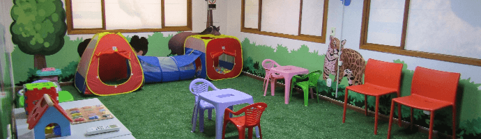 Sala fechada com grama sintética e ilustrações de animais nas paredes. O local conta com brinquedos infantis.