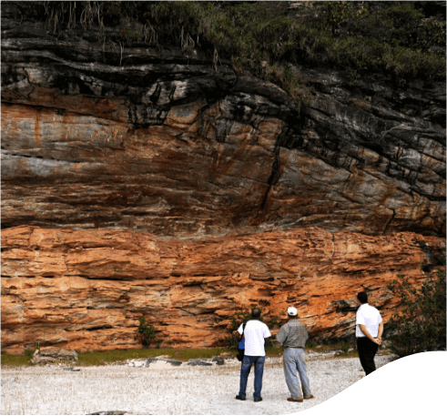 Três homens parados lado a lado olhando um grande rochedo.