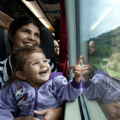 Uma mulher com uma criança no colo, eles estão em um trem e sorriem enquanto olham para janela.