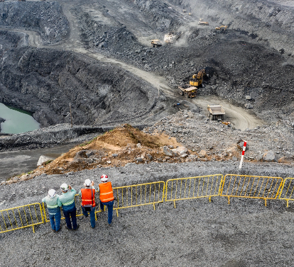 A top-down shot of four people observing an operation area near the grids. Two of them are wearing jeans, orange vests with fluorescent details and helmets. The other two are wearing jeans, green Vale shirts with some fluorescent details and helmets.