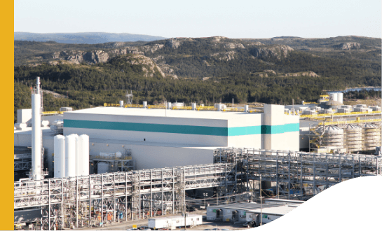 View of an industrial area, with a big warehouse, several metal structures, and in the background, a mountainous region.