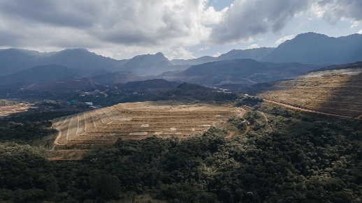Vista aérea de um campo com árvores no entorno e montanhas ao fundo