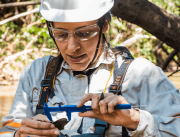 A woman, wearing goggles and a safety helmet, is using a device to measure a butterfly.