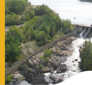 Photo of Wabageshik small hydropower plant with a concrete structure, rocks, vegetation, and moving water passing through the structures.