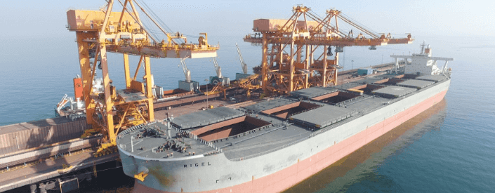 Navio cargueiro de grande porte atracado no porto de Sohar. Ao lado há cerca de três equipamento semelhantes a guindastes