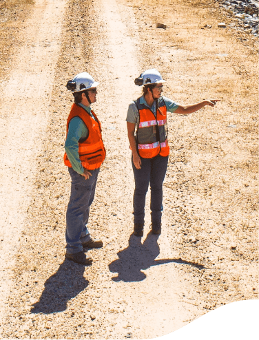 Two Vale employees on a sand floor. They are wearing orange vests and helmets. One points to the horizon and the other looks in the same direction.