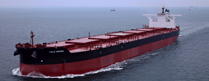 Imagem de um navio cargueiro de grande porte. Ele é vermelho e tem uma faixa preta e está navegando em alto mar.