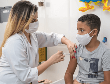 Photo of a healthcare professional holding a child's arm with one hand and applying an injection with the other. Both are wearing face masks.